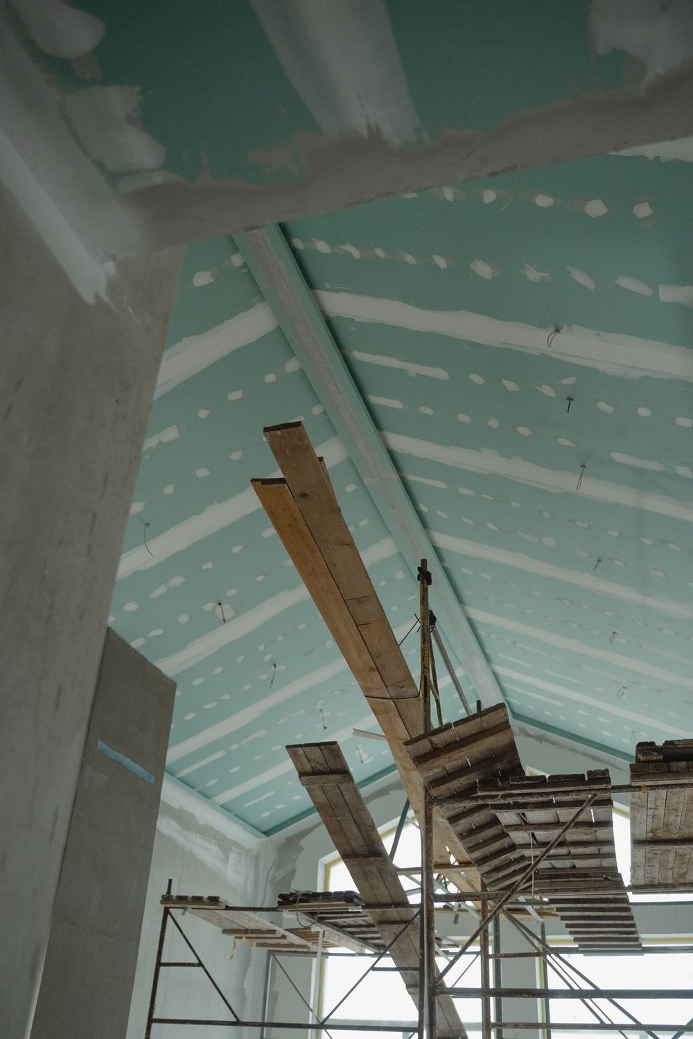 Vaulted ceiling boarded in moisture-resistant drywall with taped and filled joints, scaffold below