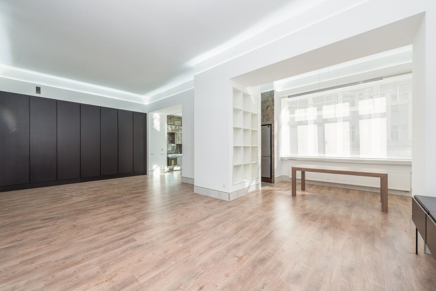 Empty finished interior with a cove-lit ceiling soffit, white built-in shelving and a dark full-height cabinet wall